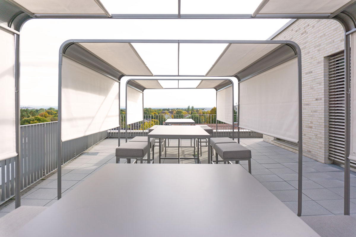 Three retractable sun awnings protecting outdoor tables and benches from sun and wind